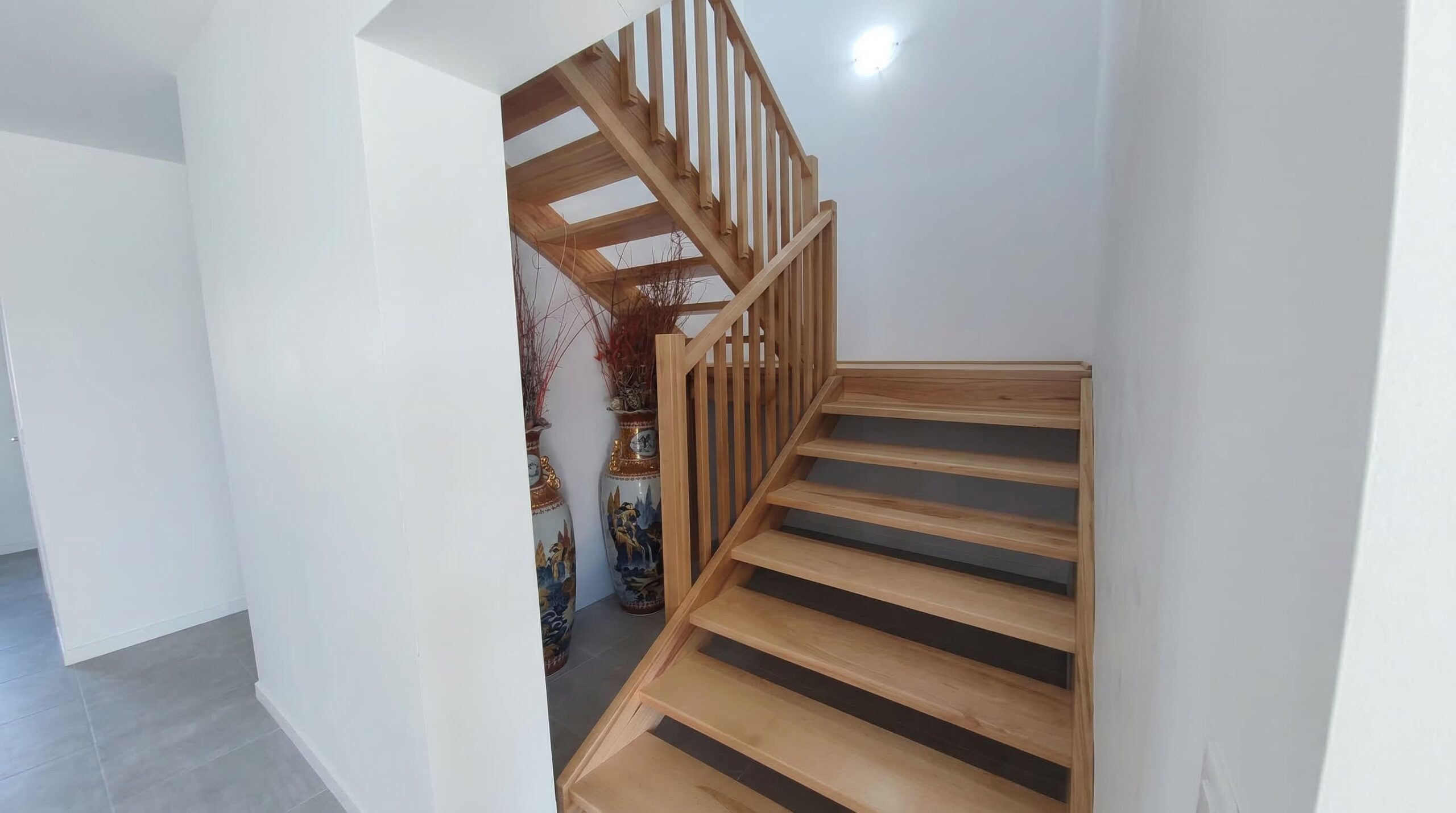 Escalera en L fabricada en madera de haya blanca instalada en un salón de concepto abierto.