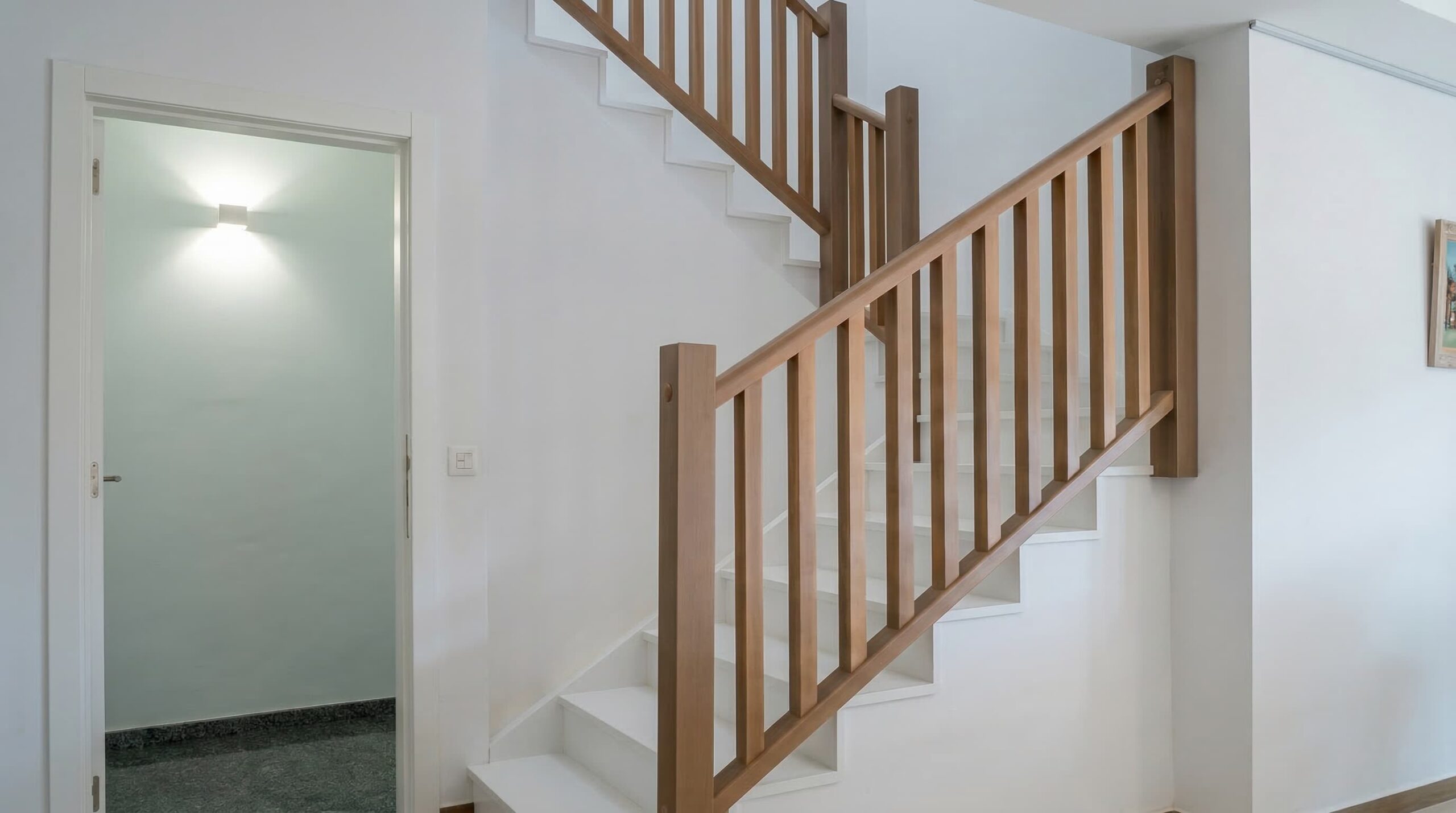 Revestimiento de una escalera de obra con peldaños blancos y barandas oscuras de madera.