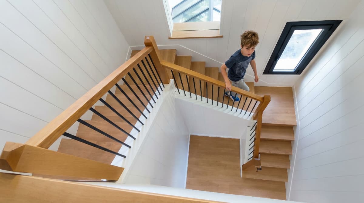 Niño bajando de forma segura por una escalera de madera tratada con barniz ecológico sin tóxicos.